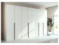 Moderner weißer Kleiderschrank mit schwarzen Griffen, Holzwand und Zimmerpflanze.