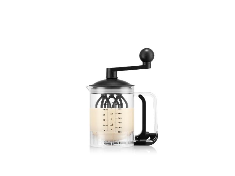 Ein klarer manueller Milchaufschäumer aus Glas mit schwarzem Griff und Deckel, der eine helle Flüssigkeit enthält.