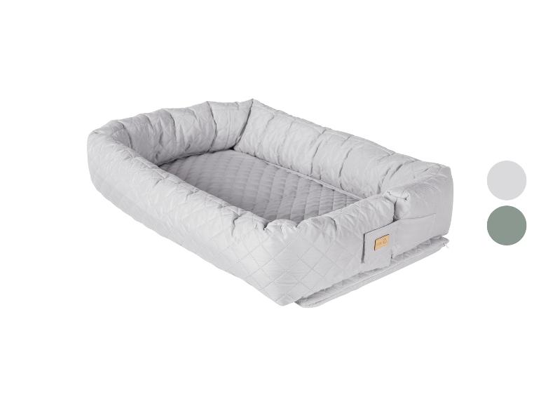 Gestepptes Babynest in Hellgrau mit kleinem Holzschild, abgebildet mit Farbmustern.