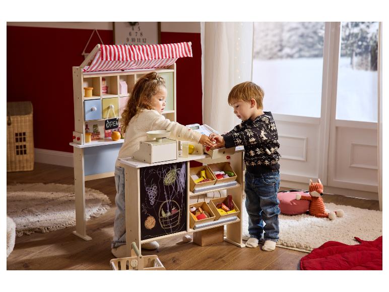 Zwei Kinder spielen mit einem hölzernen Spielzeug-Marktstand und einer Registrierkasse.