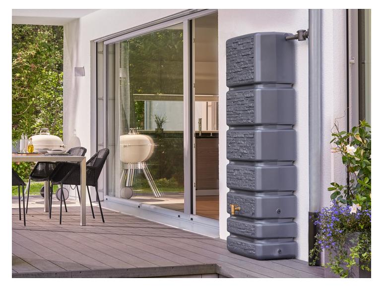 Grauer Regenspeicher auf einer Holzterrasse mit Esstisch und Grill.