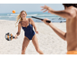 Frau im Badeanzug spielt Strandtennis mit Schläger und Ball.