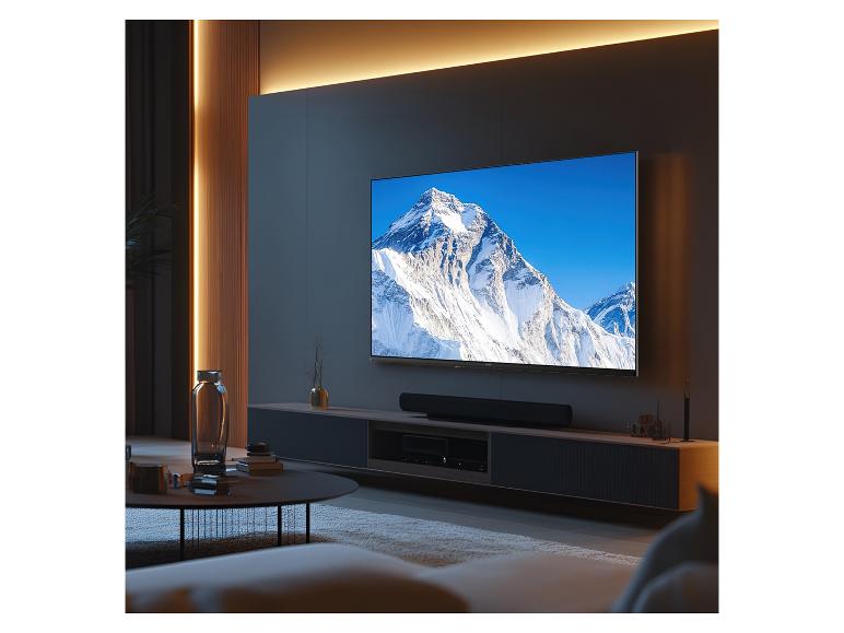 Wohnzimmer mit großem Fernseher, der eine verschneite Berglandschaft zeigt, und einer Soundbar.