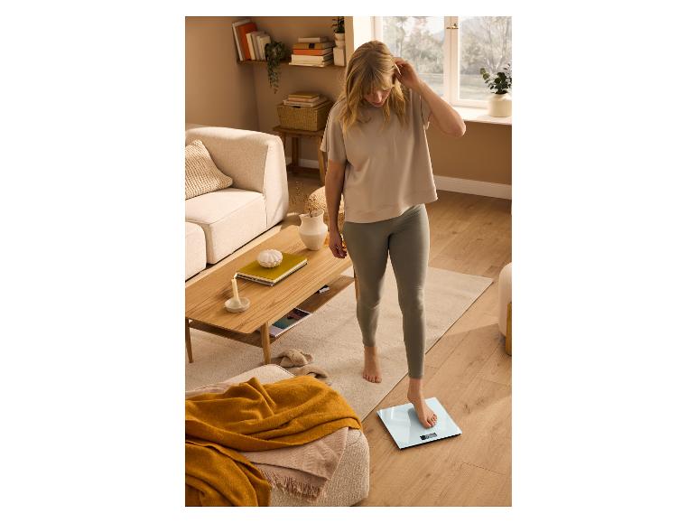 Junge Frau in T-Shirt und Leggings, wiegt sich auf einer digitalen Personenwaage.