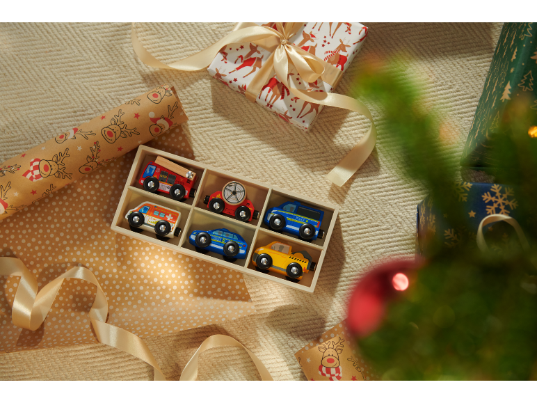 Holzspielzeugautos in einer Box, verpackte Geschenke und ein Weihnachtsbaum.