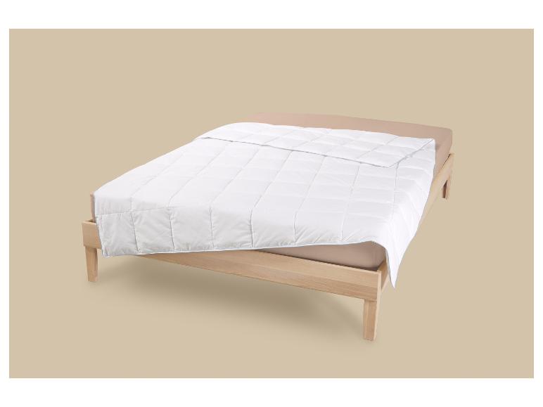 Weiße Bettdecke auf einem Holzbett mit beigem Spannbettlaken.