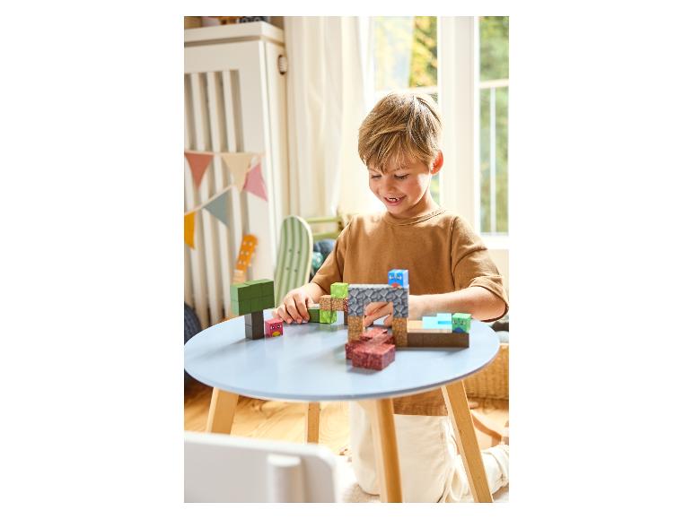 Lächelnder Junge spielt mit Minecraft-Bausteinen an einem blauen Tisch.