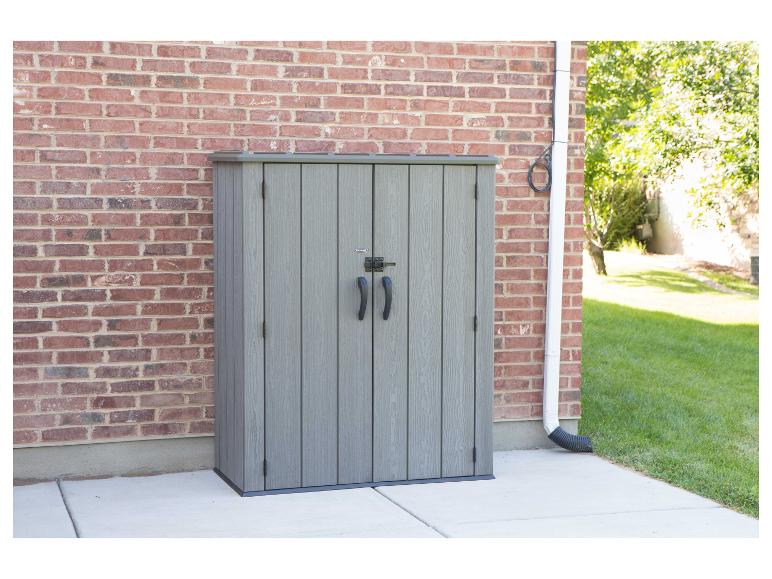 Grauer Gartenschrank mit Doppeltüren, an einer Ziegelwand stehend.