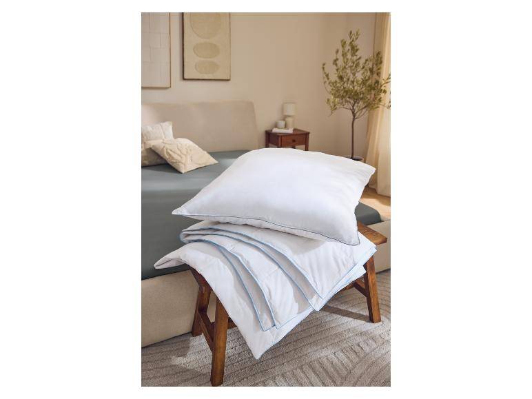 Weiße Kissen und Bettdecke mit blauem Rand auf einem Holzschemel im Schlafzimmer.