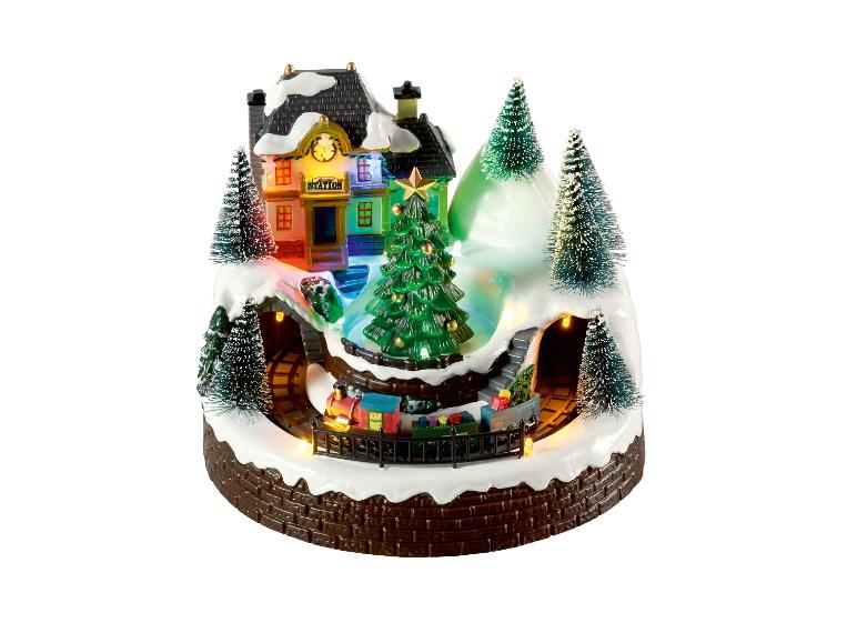 Beleuchtete Weihnachtsszene mit Zug, Bahnhof und verschneiten Bäumen.