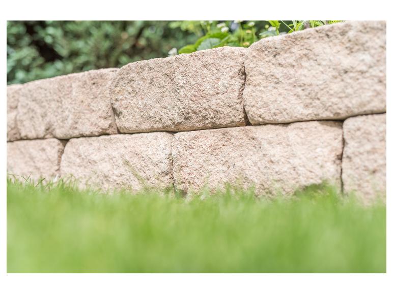 Steinmauer mit grünem Gras im Vordergrund und Grün im Hintergrund.