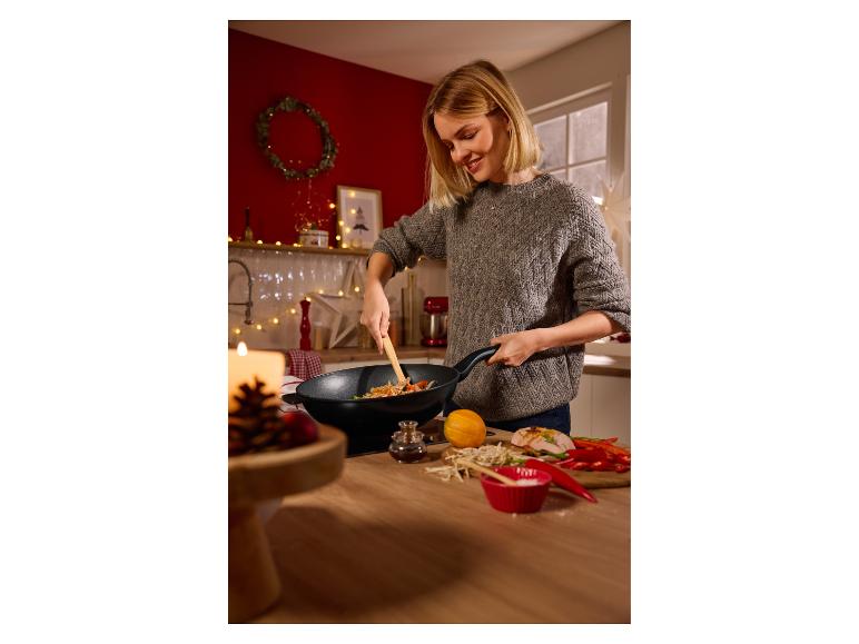 Lächelnde Frau kocht Stir-Fry im Wok, mit frischen Zutaten auf der Theke.