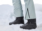 Schwarze Schneestiefel mit grauen Skianzugen im Schnee.