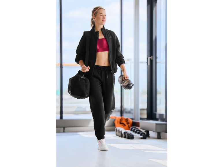 Eine Frau im schwarzen Trainingsanzug und rotem Sport-BH geht im Fitnessstudio.