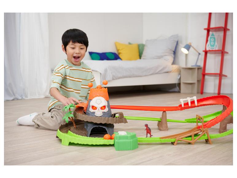 Glücklicher Junge spielt mit einem Dinosaurier-Rennbahn-Set mit Vulkan.