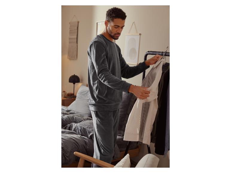 Mann in grauer Jogginghose und Pullover, der eine gestreifte Hemd betrachtet.