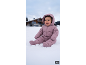 Lächelndes Baby in einem rosa Schneeanzug sitzt im Schnee mit einem Haus im Hintergrund.