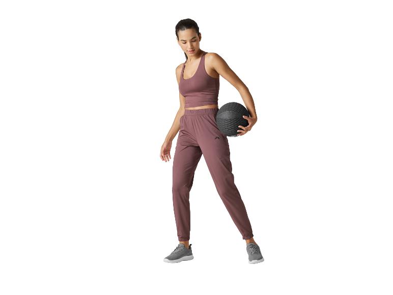 Frau in violetter Sportkleidung, hält einen schwarzen Medizinball.