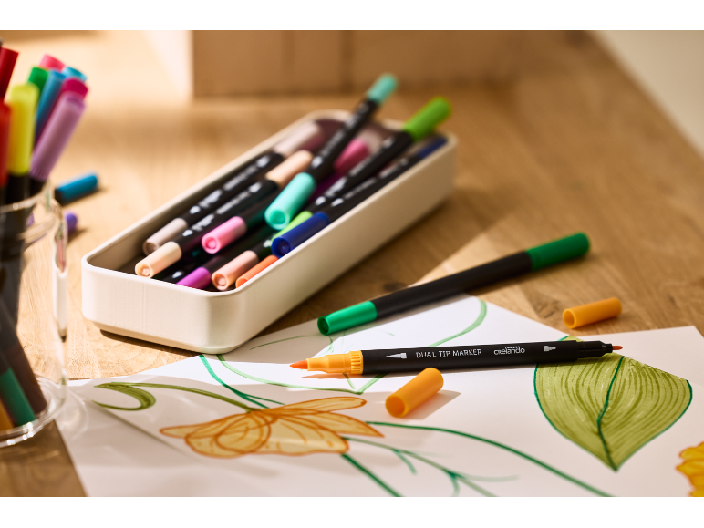 Bunte Dual-Tip-Marker und Zeichnungen auf einem Holztisch.