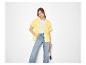 Frau in gelbem Hemd, weißem T-Shirt und weiter Jeans, mit Strohtasche.