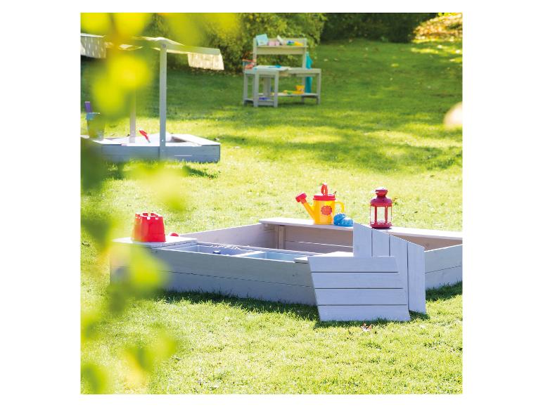 Holzsandkasten mit Sandspielzeug in einem sonnigen Garten.