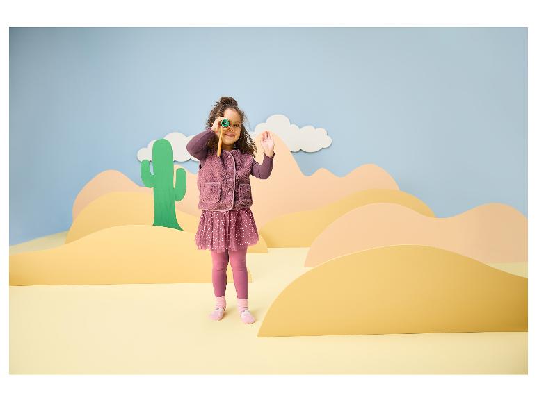 Mädchen in lila Kleidung mit Fernglas in einer Wüstenlandschaft.
