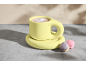 Gelbe Kakaotasse mit zwei Macarons auf Betonoberfläche.