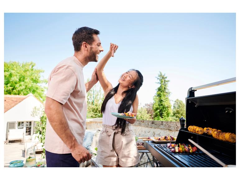Paar grillt draußen, Frau füttert Mann, Mais und Gemüsespieße auf dem Grill.