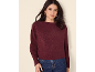 Frau in bordeauxfarbenem Pullover und blauen Jeans, goldene Ohrringe.