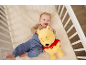 Lächelndes Baby liegt mit einem Plüschbären im Gitterbett.
