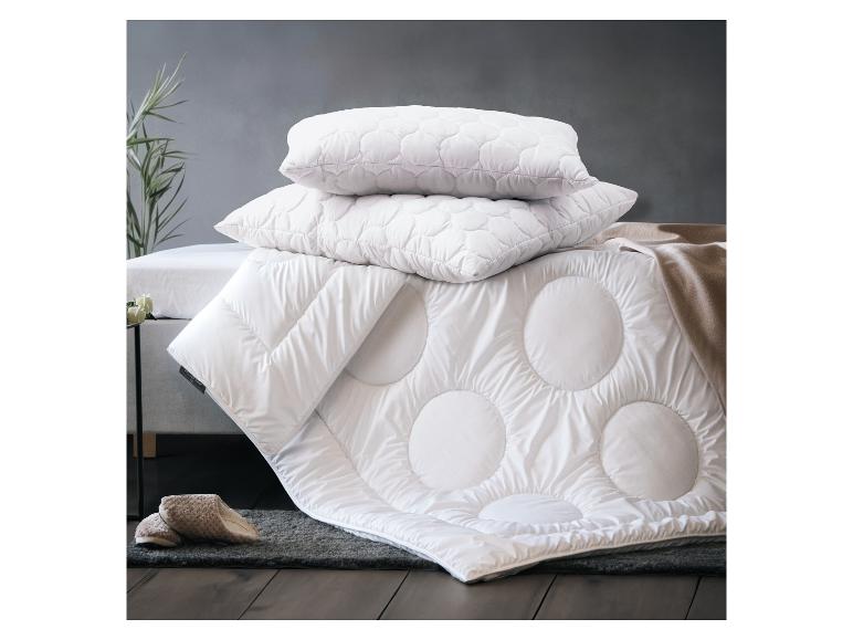 Weiße Bettwäsche und Steppdecke mit kreisförmigen Mustern auf einem Schlafzimmerboden.