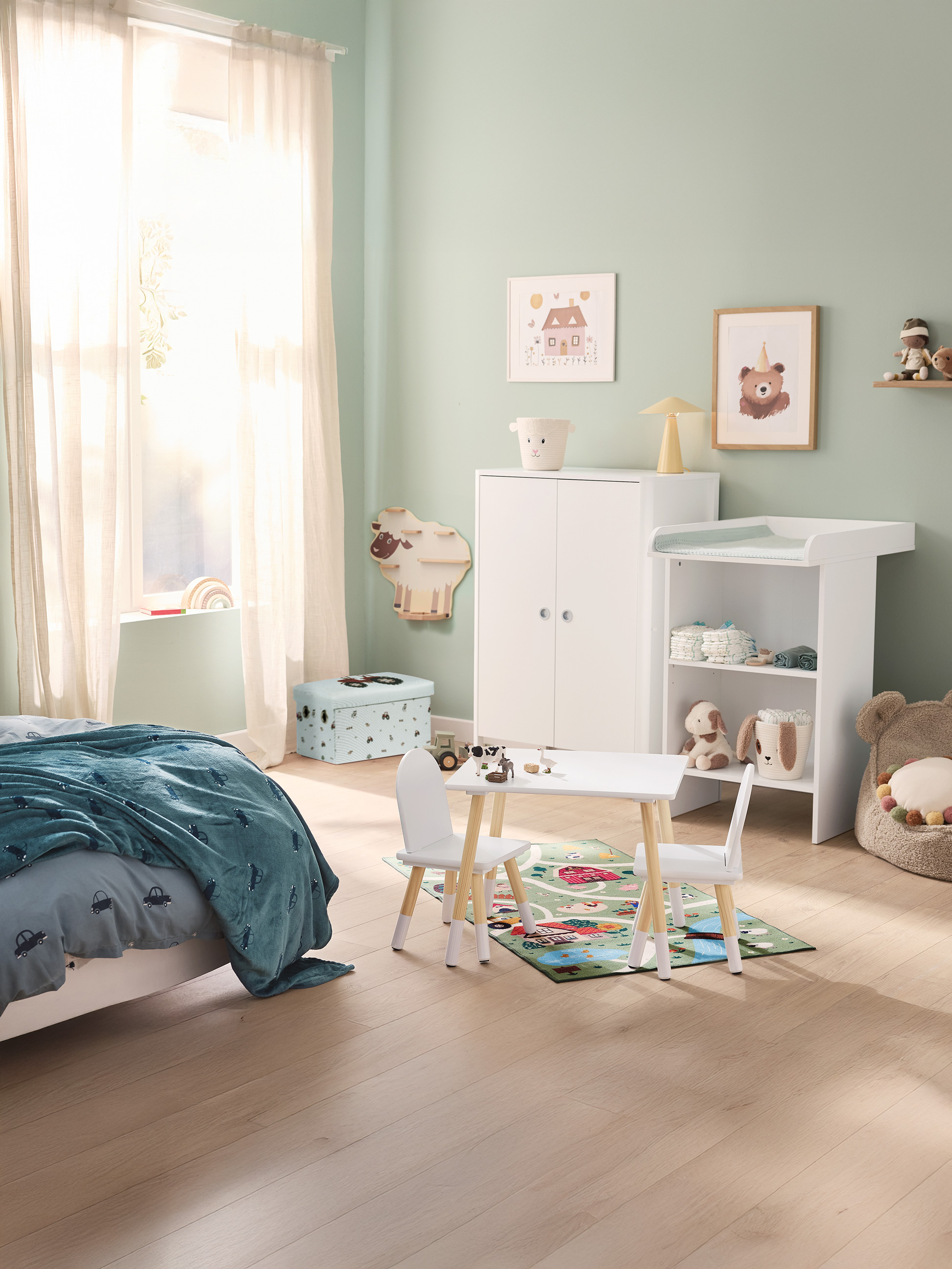 Kinderzimmer mit Bett, Tisch und Stühlen, Wickeltisch und Schrank, in Pastelltönen dekoriert.