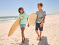 Zwei Kinder gehen am Strand mit Surfbrettern.
