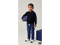 Ein Junge in einem dunkelblauen Strick-Polopullover, Cargo-Jeans und Socken hält einen blauen Block.