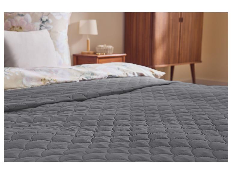 Graue Steppdecke auf einem Bett mit Blumenbettwäsche und Nachttisch