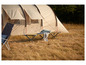 Ein Campingbett und ein Stuhl stehen vor einem Zelt auf einem Feld.