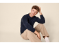 Mann in marineblauem Pullover und beiger Hose, auf dem Boden sitzend.