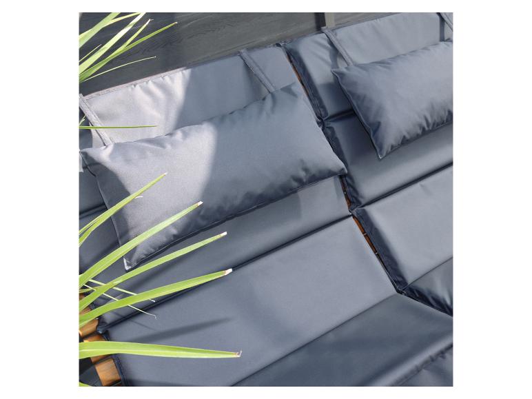 Graue Kissen und Polster auf einer Holzliege mit grünen Pflanzen.