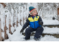 Lächelndes Kind in Skijacke und Schneehose sitzt auf verschneiten Stufen.