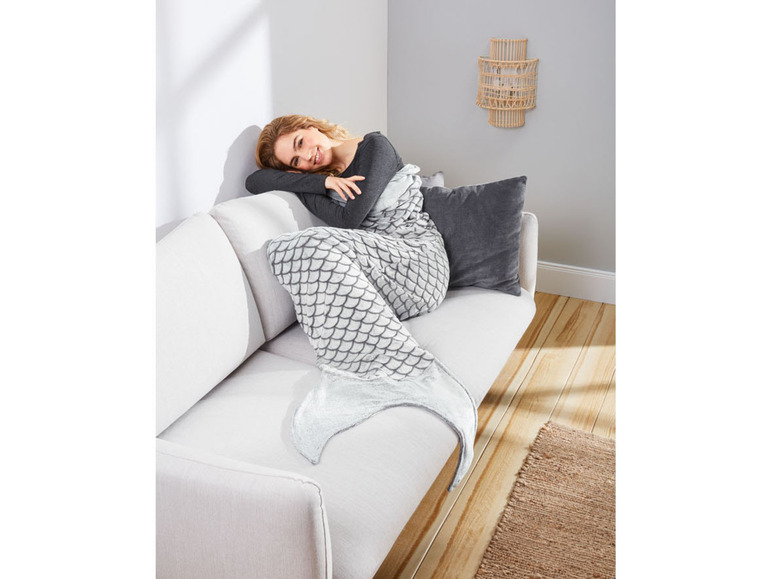 Eine Frau liegt auf einem Sofa mit einer grauen Meerjungfrauen-Decke.