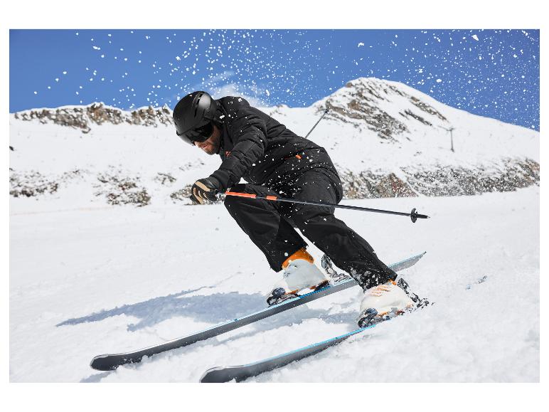 Mann fährt Ski einen verschneiten Berg hinunter, trägt schwarze Skijacke, Hose und Helm.