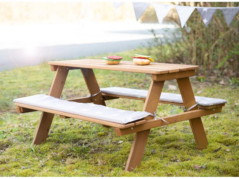 Hölzerner Kindertisch mit Kissen und Spielzeugessen im Garten.