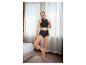 Frau in schwarzer Unterwäsche, Crop-Top und High-Waist-Slip, posiert in einem Schlafzimmer.