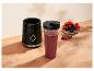 Schwarze Mixerbasis mit einem Smoothie-Becher und einer Schale frischer Beeren auf einer Holzoberfläche.