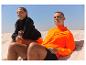 Sportbekleidung: orange Jacke und schwarzer Pulli, am Strand.