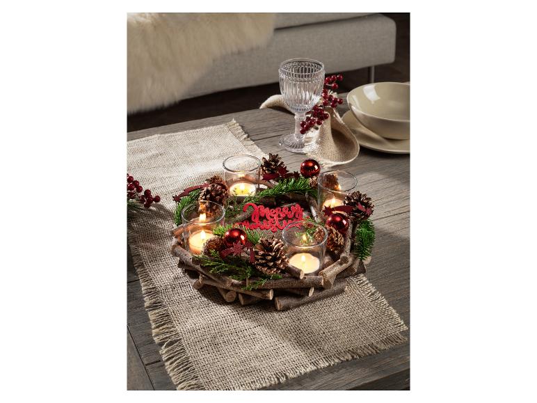 Weihnachtliches Tafelarrangement mit Kerzen, Tannenzapfen und Dekorationen auf einem Holztisch.