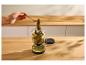 Hand nimmt eine Gewürzgurke mit einer Gabel aus einem Glas auf einer Holztheke.