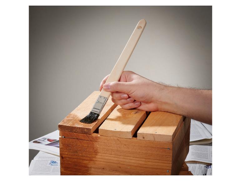 Hand lackiert eine Holzkiste mit einem Pinsel.