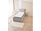 Graues Boxspringbett mit weißer Matratze in einem Schlafzimmer mit Holzboden und beigem Teppich.