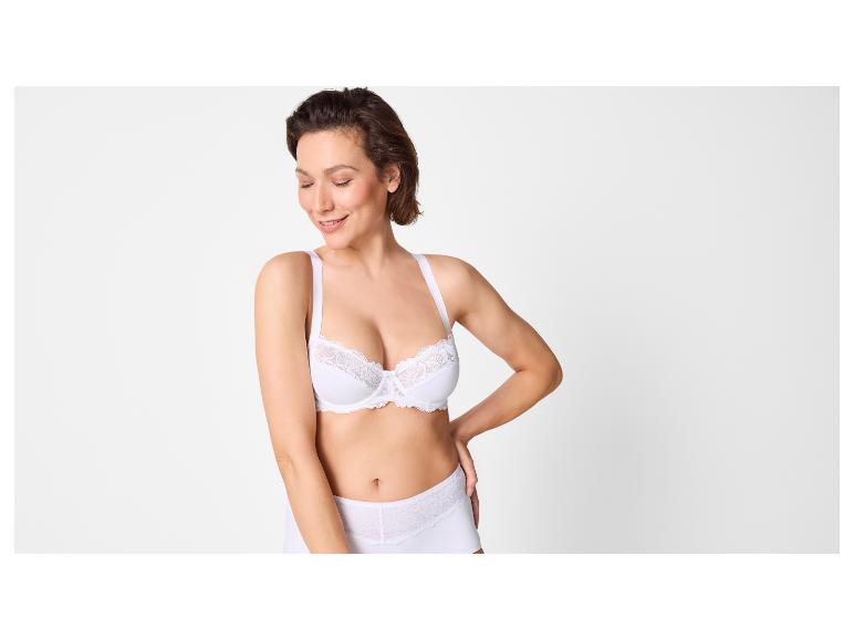 Frau in weißem BH und Slip mit Spitzendetails, lächelnd.